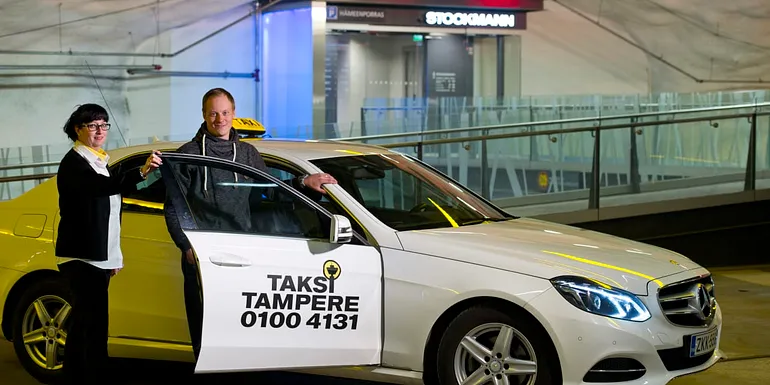 The female driver holds the taxi door open for the male customer in Stockmann parking garage.