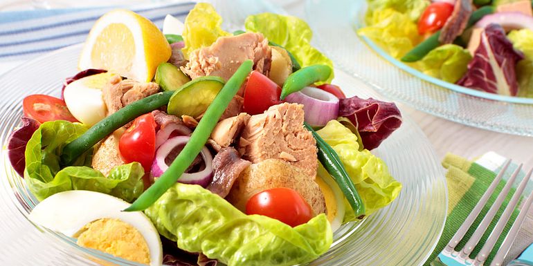 Kuva salaattilautasesta, jolla on tonnikalaa, salaatinlehtiä, kananmunaa, pikkutomaatteja ja papuja.