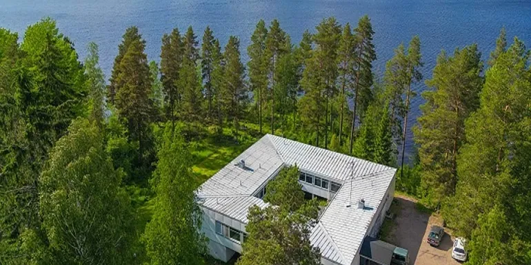 Ilmakuva Vinsanvillasta, joka sijaitsee järven rannalla ja jossa näkyvät maalaukselliset luontomaisemat sekä rakennuksen ainutlaatuinen arkkitehtuuri