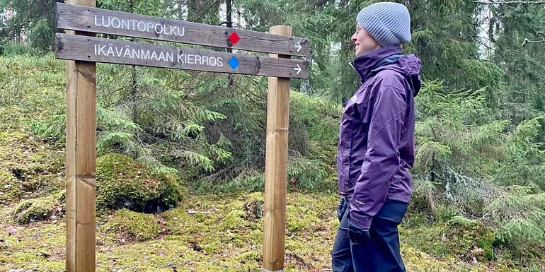 Nainen lukee luontopolun opasteviittaa metsässä.