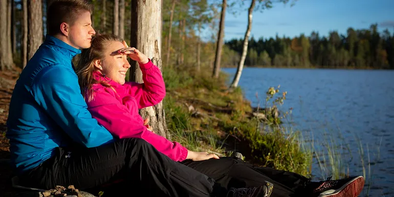 Nuoripari istuu sylikkäin järven rannalla ja katsoo horisonttiin.