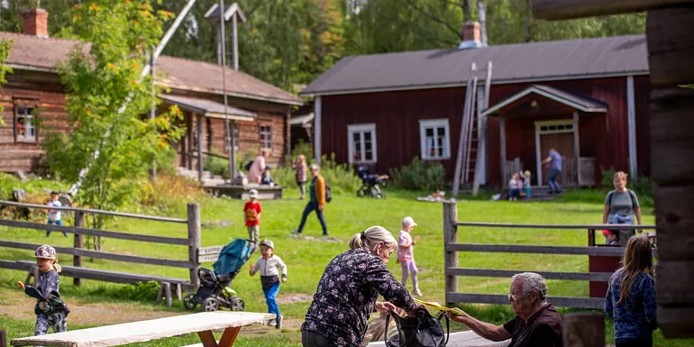 Lapsia juoksentelee Talonpoikaismuseo Yli-Kirran pihassa ja isovanhemmat katselevat menoa.