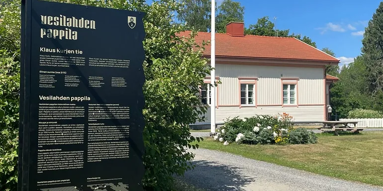 Vasemmalla edessä Klaus Kurjen tien opastetaulu, jonka taustalla näkyy Vesilahden Pappilan päärakennus.