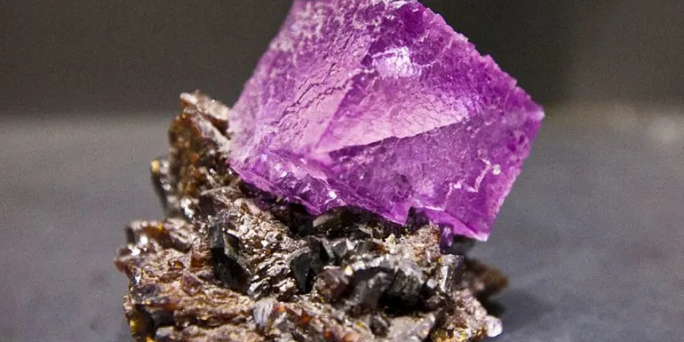 Square shaped purple amethyst stone on top of a brown mineral.