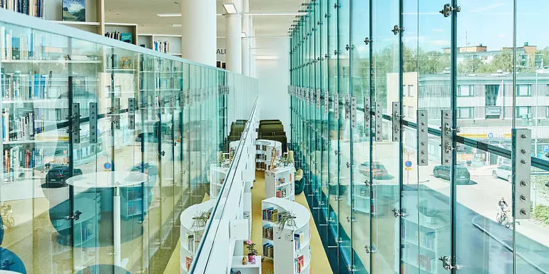 Kirjaston lasiseinän ja lasikaiteen välistä avautuu näkymä alakertaan lasten ja nuorten lukutilaan.