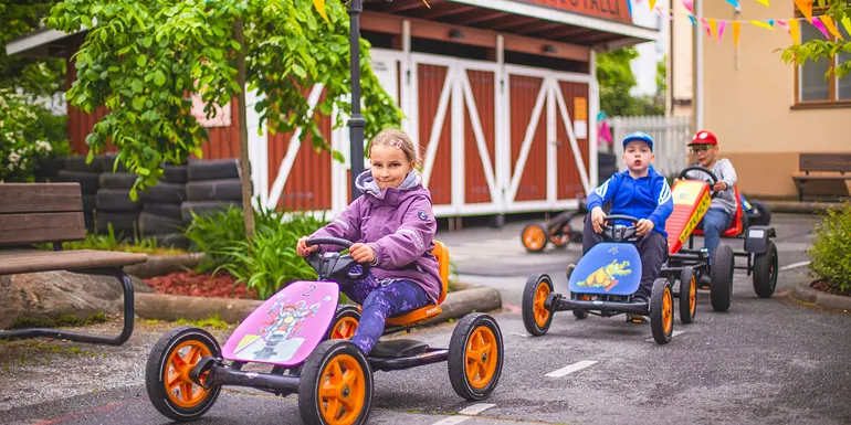 Children are driving with pedal cars in the Fun on wheels Yard.