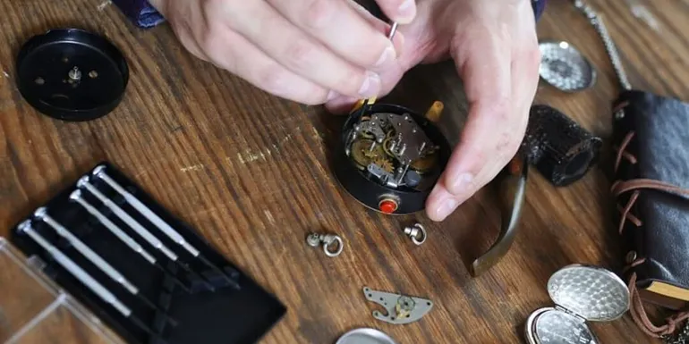 Kelloseppä työskentelee pöydän ääressä ja huoltaa avattua taskukelloa.