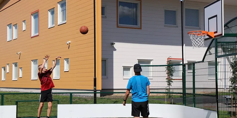 Kaksi poikaa pelaa koripalloa monitoimiareenalla.