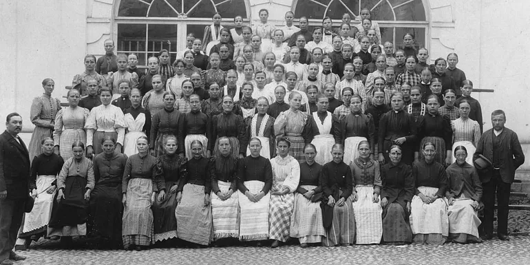 A black-and-white piciture of female factory workers in long aprons.