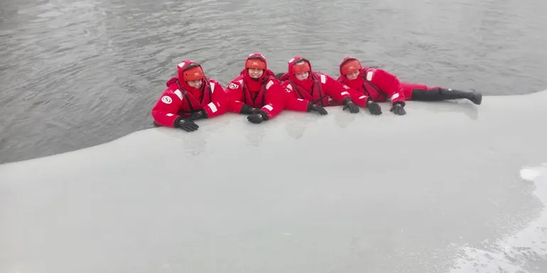 People in survival suits at the edge of the ice.