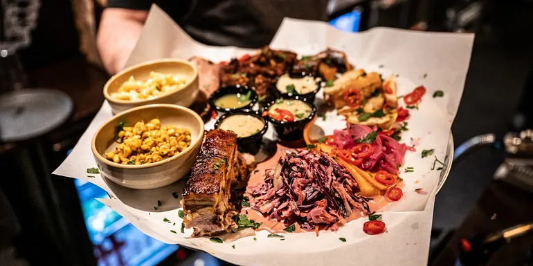 The plate features the popular Brewmaster’s Plate, which includes a selection of the restaurant’s best slow-cooked meats with side dishes. This dish is perfect for sharing between two adults.