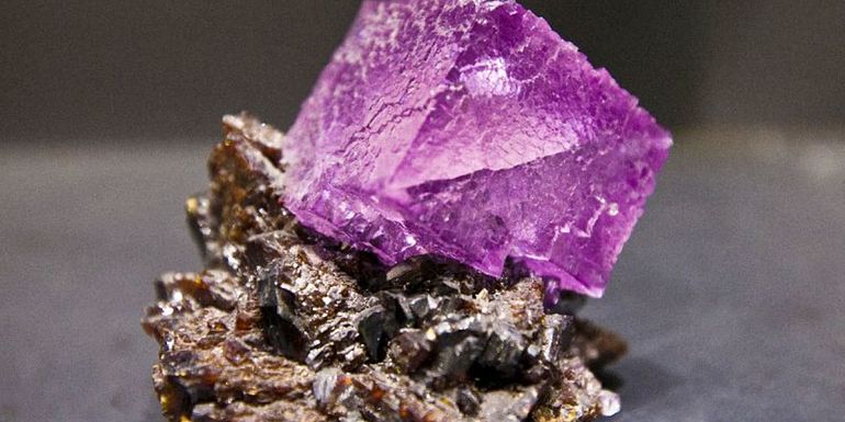 Square shaped purple amethyst stone on top of a brown mineral